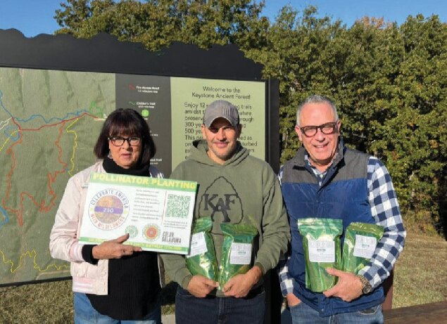 Three people holding wildflower signs in front of a shed