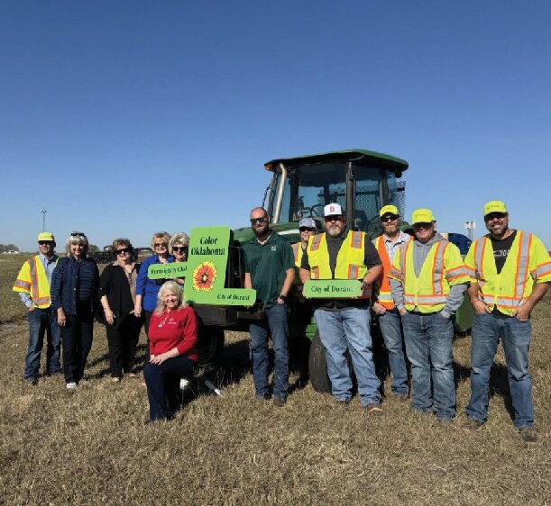 A crew in yellow safety vests standing in a freshly seeded field beside a tractor