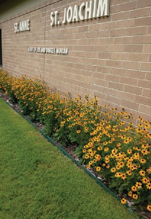 The St. Anne and St. Joachim sign on a brick wall with a bed of orange and yellow flowers below